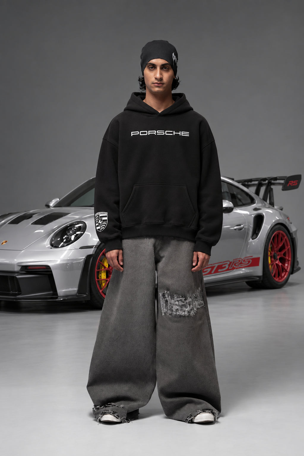 Full front view of the black Porsche hoodie beside a Porsche car